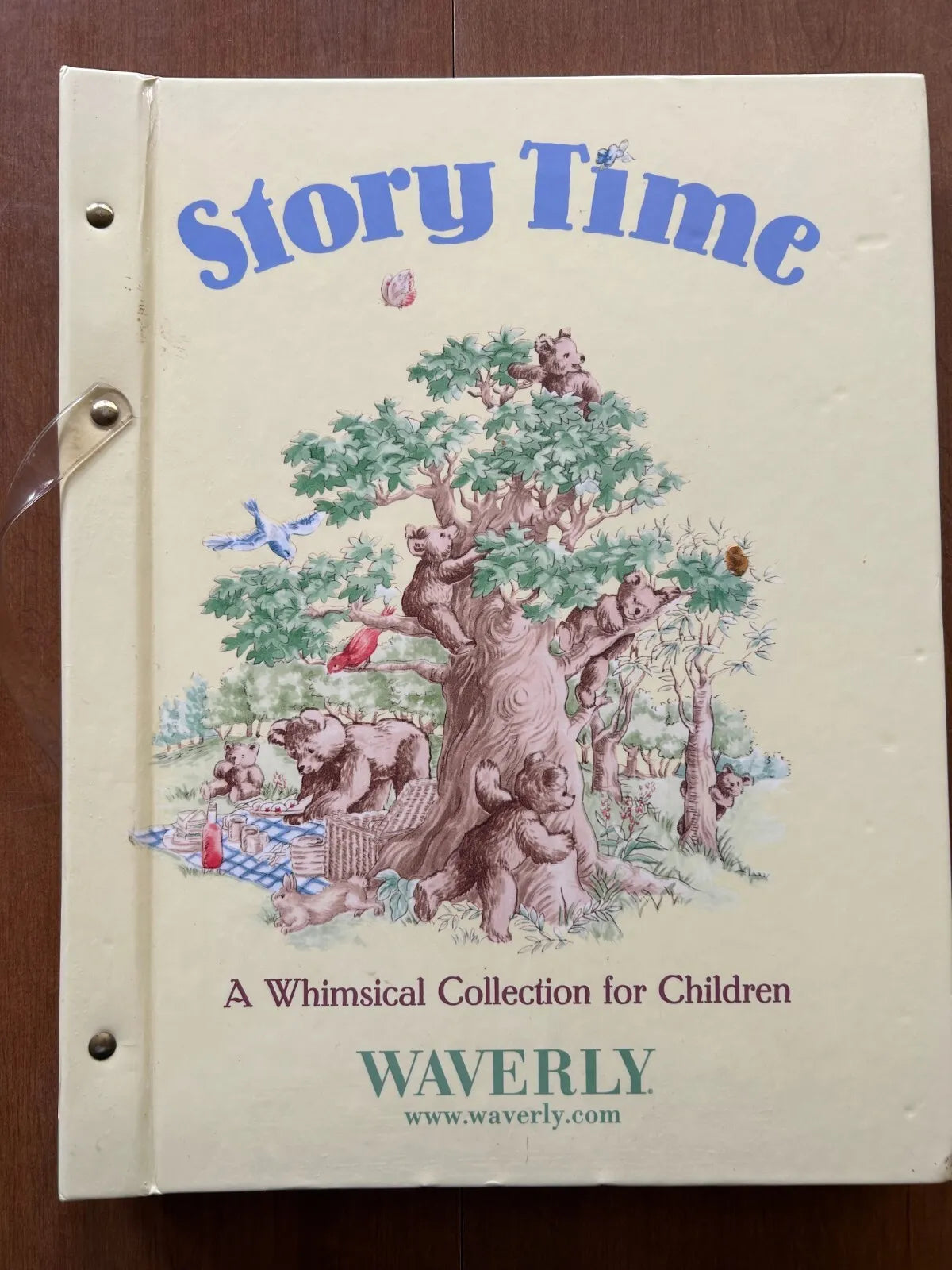 A vintage children's wallpaper sample book titled 'Story Time' by Waverly, featuring a cream-colored cover with a whimsical illustration of bears, a tree, and blue lettering, photographed on a wooden surface.